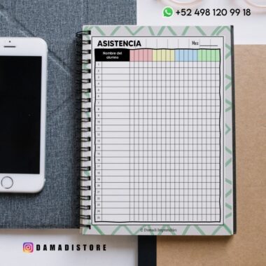 Un cuaderno de espiral abierto con una hoja de asistencia titulada "ASISTENCIA" en español, junto a un smartphone. La hoja tiene columnas para nombres, fechas y encabezados de colores, con la información de contacto y el nombre de usuario de las redes sociales visibles.