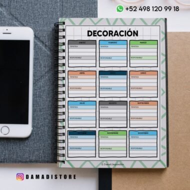 Una agenda encuadernada en espiral abierta en una página titulada "DECORACIÓN", con secciones mensuales para tareas y responsabilidades. Cerca hay un smartphone, un sobre y una carpeta marrón. También se ven los datos de contacto de Instagram y WhatsApp.