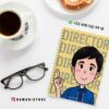 Un cuaderno de espiral con un niño ilustrado que pone "DIRECTOR" en la portada está sobre una mesa blanca junto a unas gafas, una taza de café, un donut y la información de contacto de DAMADISTORE con iconos de Instagram y WhatsApp.
