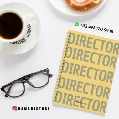 Un cuaderno de espiral con la palabra "DIRECTOR" escrita repetidamente en la portada descansa sobre una superficie blanca junto a unas gafas negras, una taza de café, un plato con un donut y datos de contacto y redes sociales.