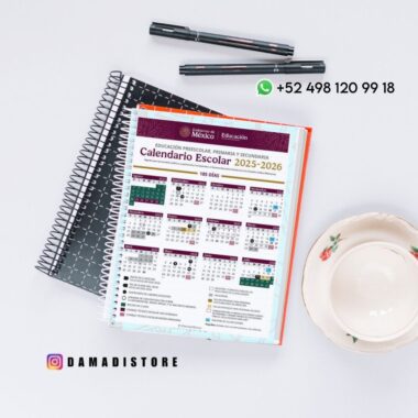 Un cuaderno de espiral con el calendario escolar mexicano 2025-2026 está abierto sobre un escritorio, junto a dos cuadernos cerrados, un bolígrafo y unas gafas. En la imagen aparecen un número de teléfono de WhatsApp y un "handle" de Instagram.