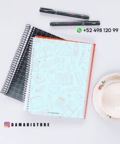 Tres cuadernos de espiral, dos bolígrafos y una taza de té con platillo sobre una superficie blanca. El cuaderno superior tiene una cubierta azul claro con ilustraciones de temática escolar. El texto de la imagen incluye un número de teléfono y una cuenta de Instagram.