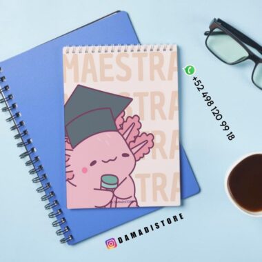 Encima de un cuaderno azul hay un cuaderno de espiral con un simpático dibujo animado de un axolotl que lleva un birrete de graduación y sostiene un diploma. Cerca hay unas gafas, una taza de café y los datos de contacto de DAMADISTORE en la imagen.