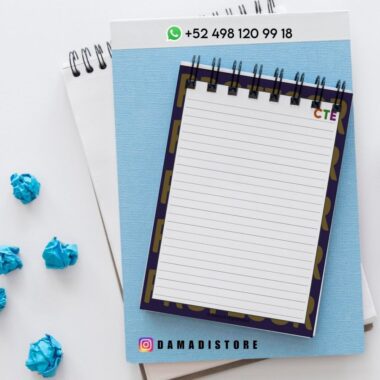 Un cuaderno de espiral con páginas rayadas está sobre una carpeta azul, rodeado de papel azul arrugado. En la parte superior e inferior de la imagen se ve un número de teléfono con un icono de WhatsApp y una cuenta de Instagram (@damadistore).