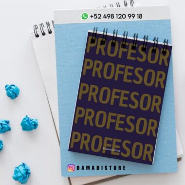 Un cuaderno de espiral con la palabra "PROFESOR" repetida en letras doradas en negrita sobre una cubierta oscura, colocada sobre blocs de notas azules y blancos. Cerca aparecen bolas de papel azul arrugado e información de contacto de DAMADISTORE.