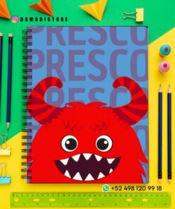 Cuaderno de espiral con un monstruo rojo de dibujos animados y dientes afilados en la portada, rodeado de lápices, clips, gomas de borrar y origami de colores sobre un fondo amarillo y verde.