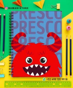 Un cuaderno de espiral con un monstruo rojo de dibujos animados y grandes dientes en la portada, rodeado de lápices de colores, clips, papel y una regla amarilla sobre un fondo azul y amarillo. La información de contacto de Damadistore es visible.